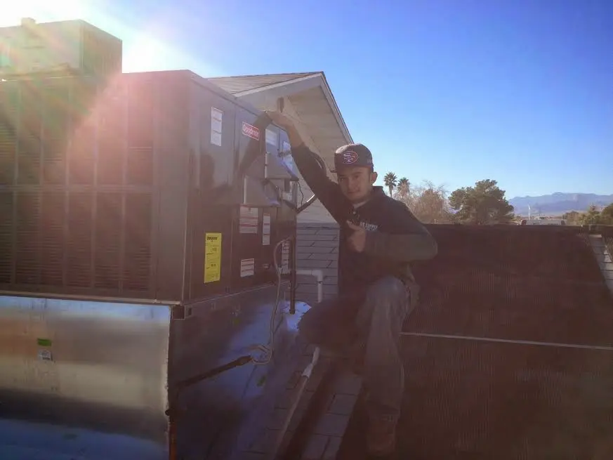 HVAC technician performing Air Duct Cleaning on a rooftop unit in Genoa